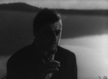Movie still from “Nights of Cabiria” (1957), directed by Federico Fellini – A black and white photo of a man smoking a cigarette; Close Up shot, High angle