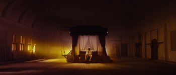 Movie still from “Nightwatching” (2007), directed by Peter Greenaway – A person sitting on a stage with a wagon; Wide shot, Low angle
