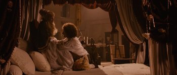 Movie still from “Nightwatching” (2007), directed by Peter Greenaway – A woman sitting on a bed next to a doll; Wide shot, Overhead angle
