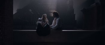 Movie still from “Nightwatching” (2007), directed by Peter Greenaway – A man and a woman sitting on a ledge holding a baby; Wide shot, High angle