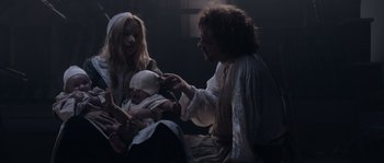 Movie still from “Nightwatching” (2007), directed by Peter Greenaway – A man holding a baby in his arms while sitting next to a woman; Medium shot, High angle