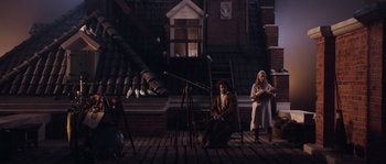 Movie still from “Nightwatching” (2007), directed by Peter Greenaway – A man and a woman sitting in front of a telescope; Wide shot, High angle