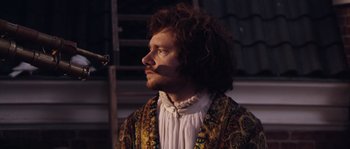 Movie still from “Nightwatching” (2007), directed by Peter Greenaway – A man with long curly hair wearing a white shirt; Close Up shot, Over the shoulder angle