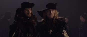 Movie still from “Nightwatching” (2007), directed by Peter Greenaway – A couple of men wearing hats and standing next to each other; Medium shot, Low angle