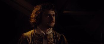 Movie still from “Nightwatching” (2007), directed by Peter Greenaway – A man with a beard and curly hair wearing a yellow and black outfit; Close Up shot, Over the shoulder angle