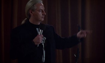 Movie still from “Nil by Mouth” (1997), directed by Gary Oldman – A man with long blonde hair holding a pair of scissors; Medium shot, Over the shoulder angle