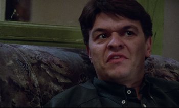 Movie still from “Nil by Mouth” (1997), directed by Gary Oldman – A person sitting on a couch with his eyes wide open; Close Up shot, Low angle