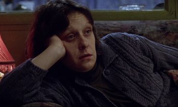 Movie still from “Nil by Mouth” (1997), directed by Gary Oldman – A woman sitting on a couch with her head resting on her hand; Close Up shot, High angle