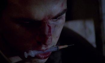 Movie still from “Nil by Mouth” (1997), directed by Gary Oldman – A person holding a syringe in his mouth; Extreme Close Up shot, Overhead angle