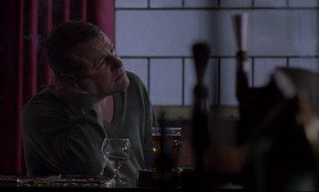 Movie still from “Nil by Mouth” (1997), directed by Gary Oldman – A man sitting at a table with a glass of wine; Medium shot, Low angle