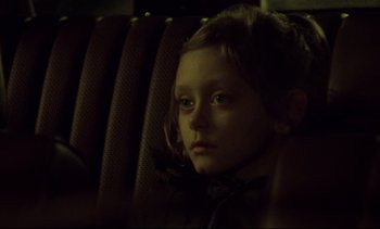 Movie still from “Nil by Mouth” (1997), directed by Gary Oldman – A young girl sitting in a car seat looking at the camera; Close Up shot, Over the shoulder angle