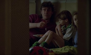 Movie still from “Nil by Mouth” (1997), directed by Gary Oldman – A man sitting next to a boy eating pizza; Medium shot, High angle