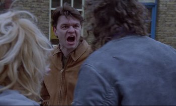 Movie still from “Nil by Mouth” (1997), directed by Gary Oldman – A man with his mouth wide open in front of a group of people; Close Up shot, Over the shoulder angle