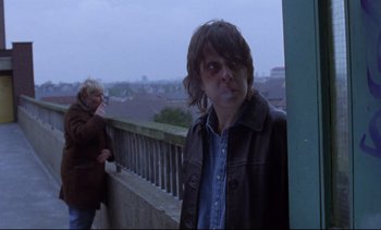 Movie still from “Nil by Mouth” (1997), directed by Gary Oldman – A woman standing on a balcony next to a man; Medium shot, Over the shoulder angle