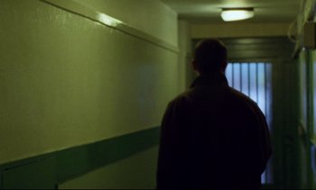 Movie still from “Nil by Mouth” (1997), directed by Gary Oldman – A man walking down a hallway in a building; Medium shot, Low angle