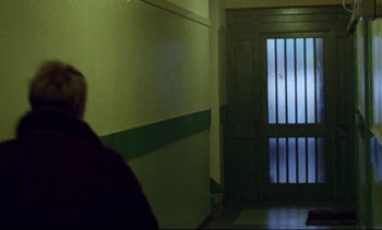 Movie still from “Nil by Mouth” (1997), directed by Gary Oldman – A man standing next to a door in a room; Wide shot, Low angle