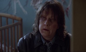 Movie still from “Nil by Mouth” (1997), directed by Gary Oldman – A person with a leather jacket on sitting in front of a chair; Close Up shot, Low angle