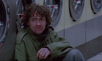 Movie still from “Nil by Mouth” (1997), directed by Gary Oldman – A man sitting in front of a washing machine; Medium shot, Low angle