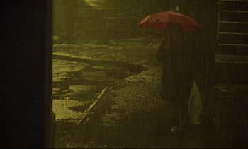Movie still from “Nil by Mouth” (1997), directed by Gary Oldman – A person holding an open umbrella in the rain; Wide shot, High angle