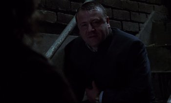 Movie still from “Nil by Mouth” (1997), directed by Gary Oldman – A man in a suit sitting on a stair case; Medium shot, Low angle