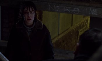 Movie still from “Nil by Mouth” (1997), directed by Gary Oldman – A person standing in a dark room near a wall; Close Up shot, Over the shoulder angle