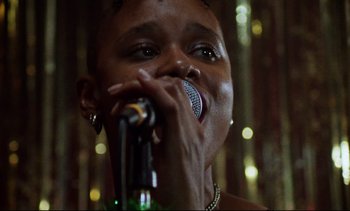 Movie still from “Nil by Mouth” (1997), directed by Gary Oldman – A woman singing into a microphone with a bottle in front of her face; Close Up shot, Low angle