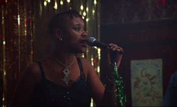 Movie still from “Nil by Mouth” (1997), directed by Gary Oldman – A woman is singing into a microphone in front of a crowd; Medium shot, Low angle