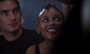 Movie still from “Nil by Mouth” (1997), directed by Gary Oldman – A person smiling with a person in the background; Close Up shot, Over the shoulder angle