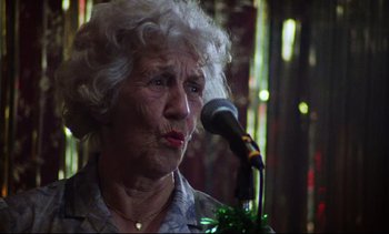 Movie still from “Nil by Mouth” (1997), directed by Gary Oldman – An older woman is speaking into a microphone; Close Up shot, Over the shoulder angle