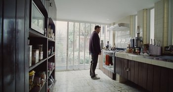 Movie still from “Nimic” (2019), directed by Yorgos Lanthimos – A man standing in a kitchen next to an oven; Wide shot, High angle