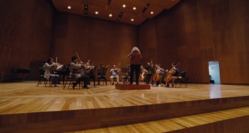 Movie still from “Nimic” (2019), directed by Yorgos Lanthimos – A group of people sitting in a room with instruments; Extreme Wide shot, Low angle
