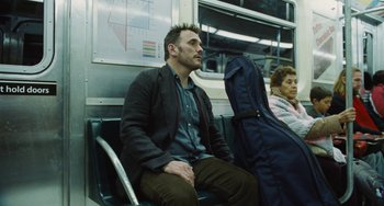 Movie still from “Nimic” (2019), directed by Yorgos Lanthimos – A man sitting on a train with a guitar case; Medium shot, Over the shoulder angle