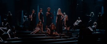 Movie still from “Nine” (2009), directed by Rob Marshall – A group of women sitting on some steps in a dark room; Wide shot, High angle