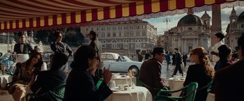 Movie still from “Nine” (2009), directed by Rob Marshall – Two people sitting at an outdoor table with plates of food; Wide shot, Over the shoulder angle