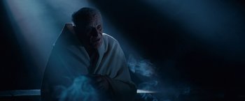 Movie still from “Nine” (2009), directed by Rob Marshall – An old man sitting in a dark room with smoke coming out of his mouth; Medium shot, Low angle