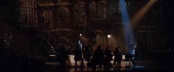 Movie still from “Nine” (2009), directed by Rob Marshall – A group of people sitting at a table in front of a building; Wide shot, Over the shoulder angle