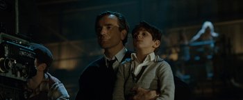 Movie still from “Nine” (2009), directed by Rob Marshall – A man standing next to a young boy in a dark room; Medium shot, Low angle