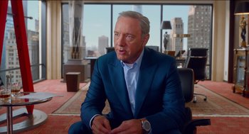 Movie still from “Nine Lives” (2016), directed by Barry Sonnenfeld – A man in a blue suit sitting in front of a window; Medium shot, Over the shoulder angle