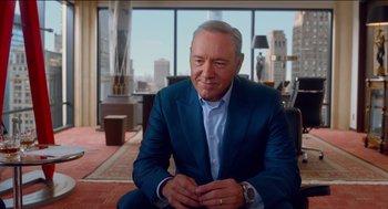 Movie still from “Nine Lives” (2016), directed by Barry Sonnenfeld – A man in a blue suit sitting in a living room; Medium shot, Over the shoulder angle