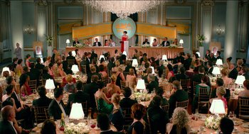 Movie still from “Nine Lives” (2016), directed by Barry Sonnenfeld – A group of people sitting at tables in front of a microphone; Extreme Wide shot, High angle
