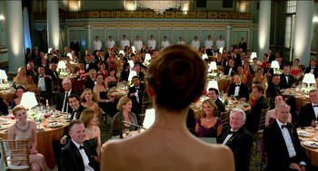Movie still from “Nine Lives” (2016), directed by Barry Sonnenfeld – A woman standing in front of a crowd of people in formal wear; Wide shot, Over the shoulder angle