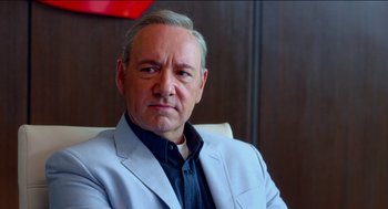 Movie still from “Nine Lives” (2016), directed by Barry Sonnenfeld – A man in a suit and tie sitting in front of a wooden wall; Close Up shot, Over the shoulder angle