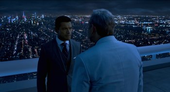 Movie still from “Nine Lives” (2016), directed by Barry Sonnenfeld – Two men in suits are standing in front of a city at night; Medium shot, Over the shoulder angle