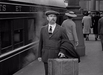 Movie still from “Ninotchka” (1939), directed by Ernst Lubitsch – A man in a suit and hat holding a suitcase; Medium shot, Over the shoulder angle