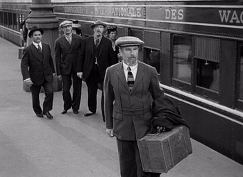 Movie still from “Ninotchka” (1939), directed by Ernst Lubitsch – A group of men walking down a train platform with suitcases; Wide shot, Low angle