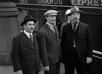 Movie still from “Ninotchka” (1939), directed by Ernst Lubitsch – A group of men standing next to each other wearing hats; Medium shot, Low angle