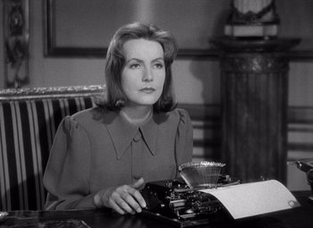 Movie still from “Ninotchka” (1939), directed by Ernst Lubitsch – A woman sitting at a table with a typewriter; Close Up shot, High angle