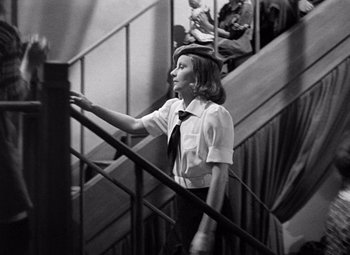 Movie still from “Ninotchka” (1939), directed by Ernst Lubitsch – A woman in white shirt and black tie walking up stairs; Medium shot, Low angle
