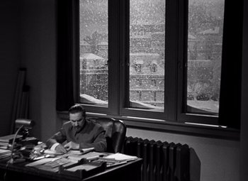 Movie still from “Ninotchka” (1939), directed by Ernst Lubitsch – A man sitting at a desk in front of a window; Wide shot, High angle