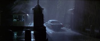Movie still from “Nixon” (1995), directed by Oliver Stone – A car is parked in the rain on the side of the road; Extreme Wide shot, Low angle